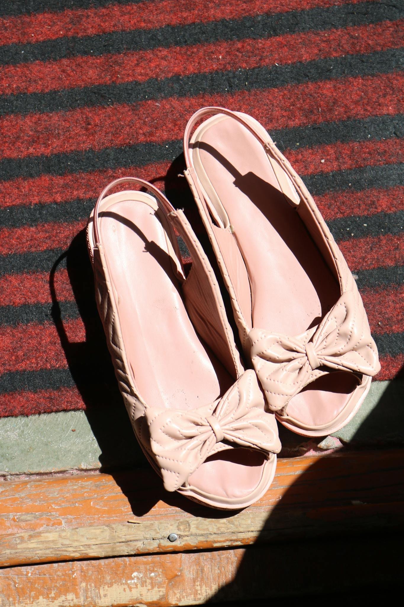 Pink open-toe shoes with bows displayed on a striped rug, capturing a stylish vibe.