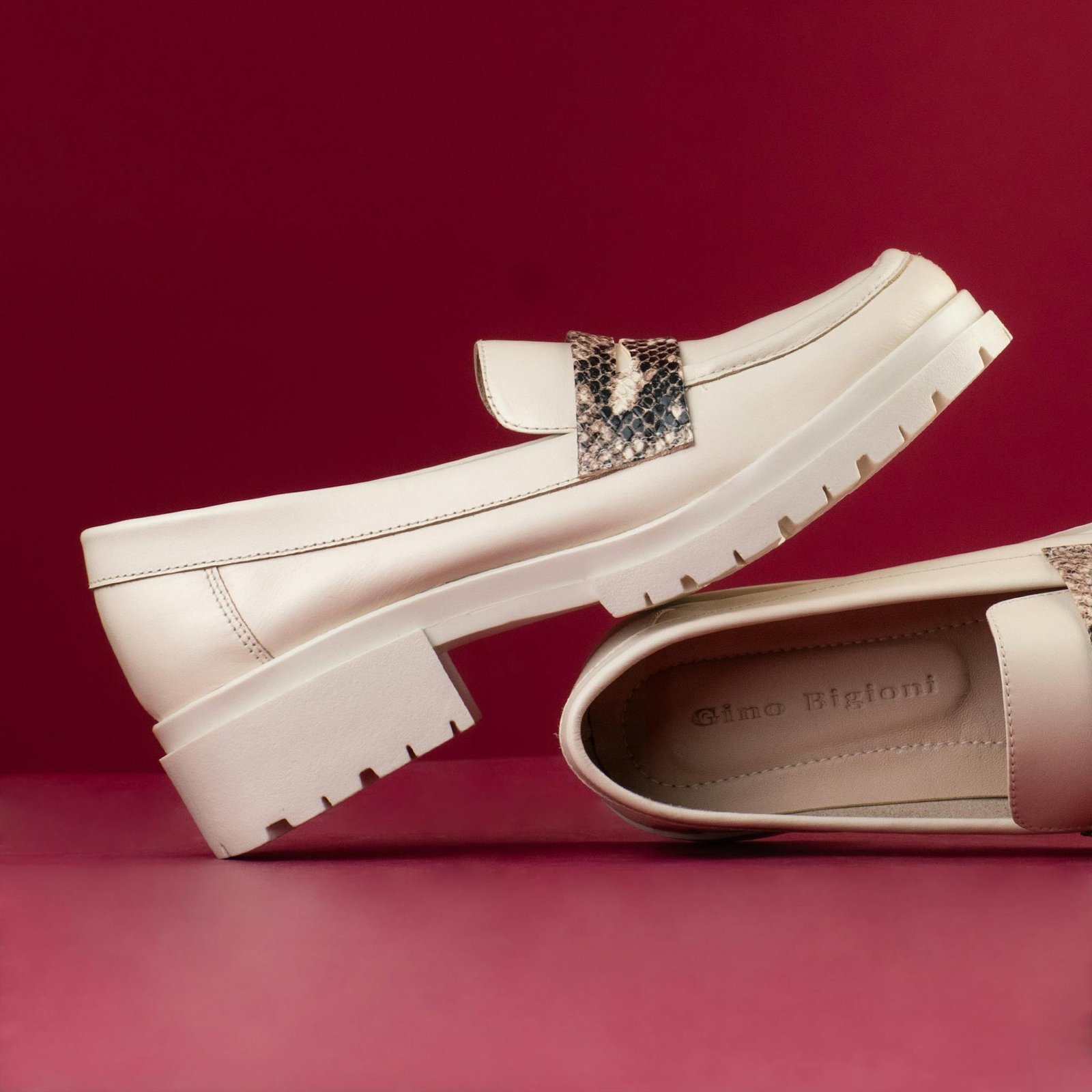 Stylish beige loafers with textured accents against a red backdrop.